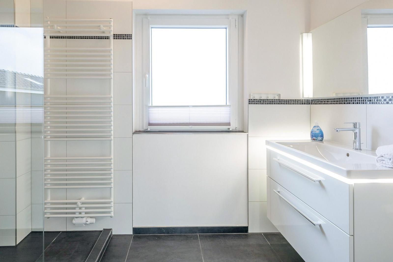 Badezimmer mit Dusche, Waschbecken und Fenster.