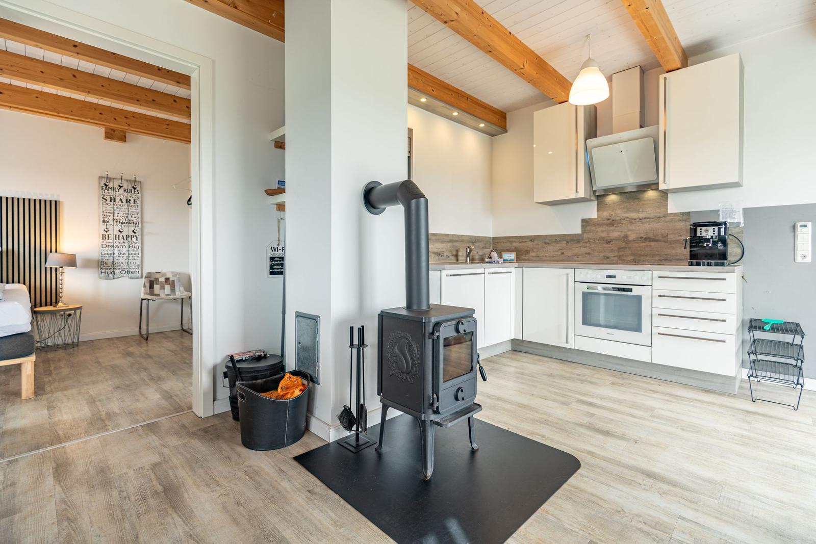 Küche mit Holzdecke, Holzfußboden und Kaminofen. Schlafzimmer im Hintergrund.