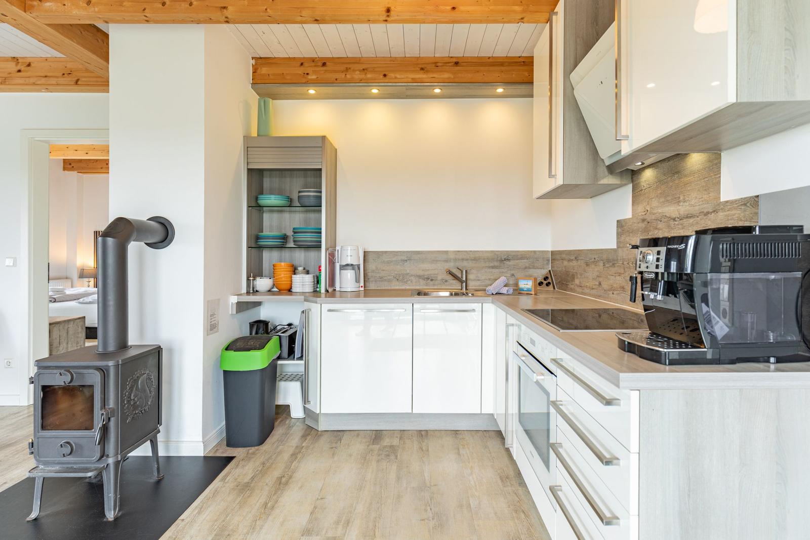 Küche mit weißen Schränken, Holzboden und Holzdecken. Links steht ein Holzofen.