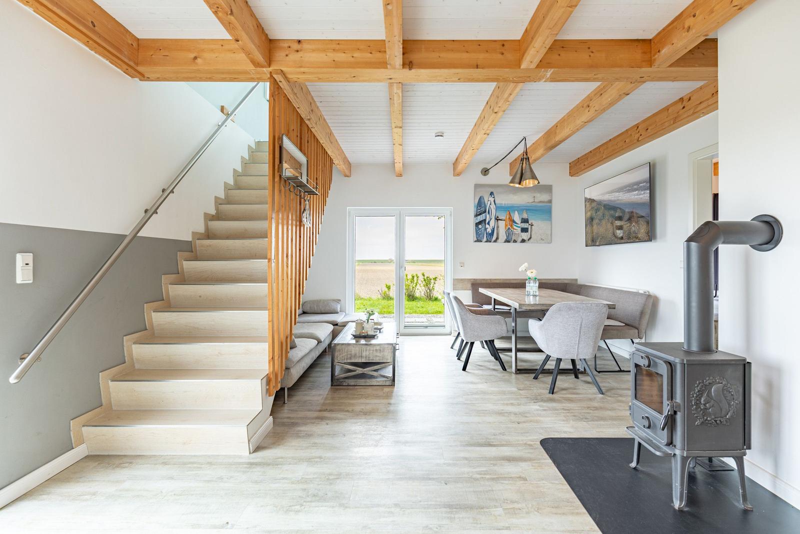 Haus mit Holzdecken, Treppe, Esstisch und Kaminofen. Blick auf grüne Landschaft.