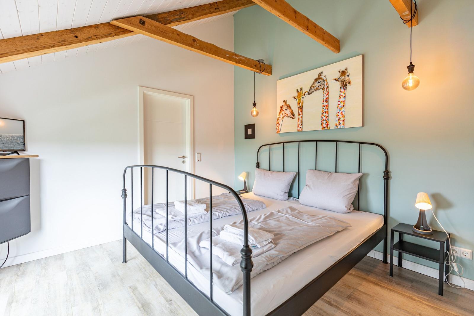 Schlafzimmer mit Bett, Wandbild und Holzbalken an der Decke.