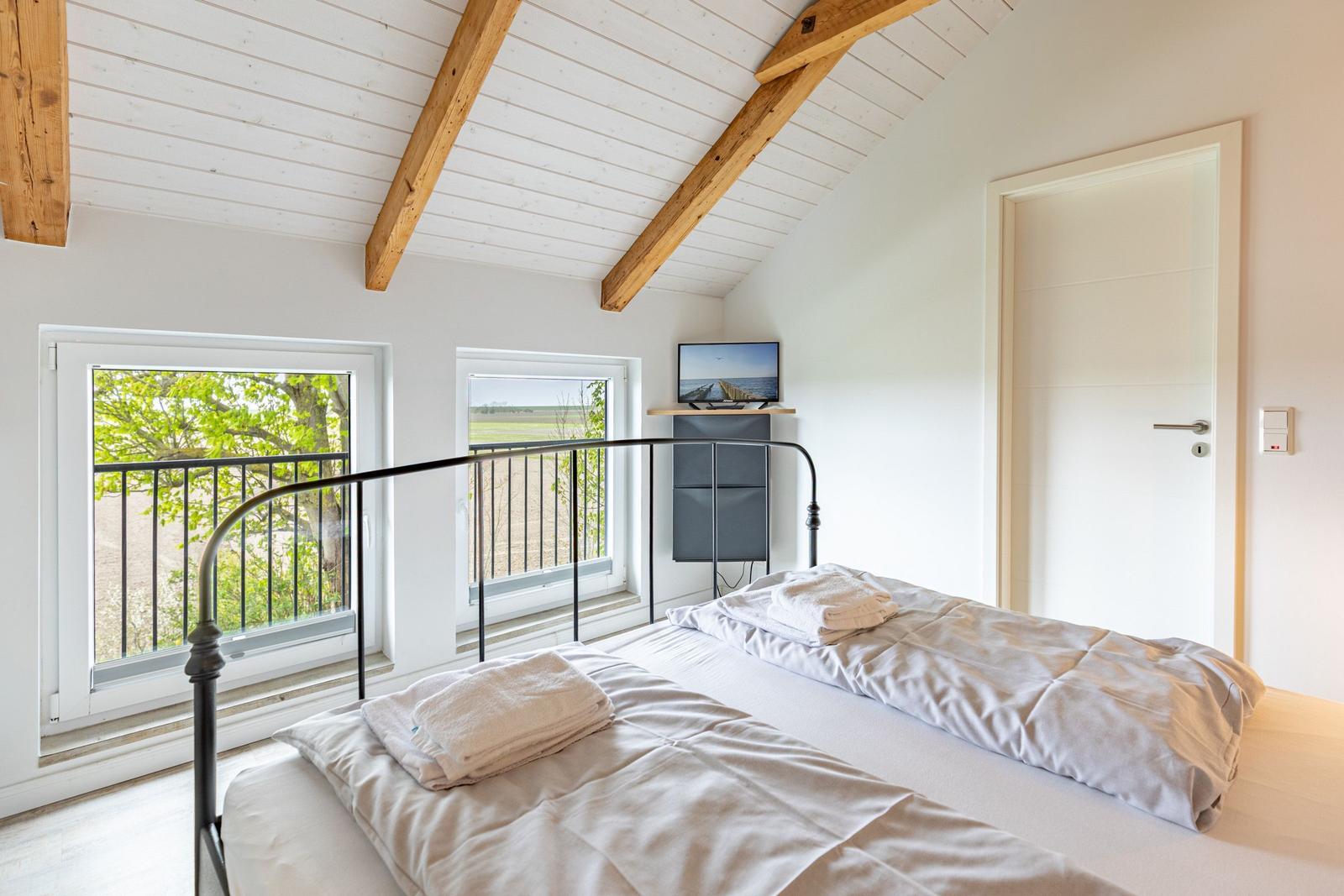 Schlafzimmer mit Doppelbett, Holzbalkendecke und Fenstern zum Balkon.