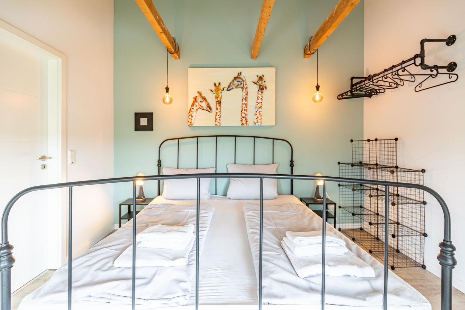Schlafzimmer mit Bett, Giraffenbild und Holzbalken an der Decke.