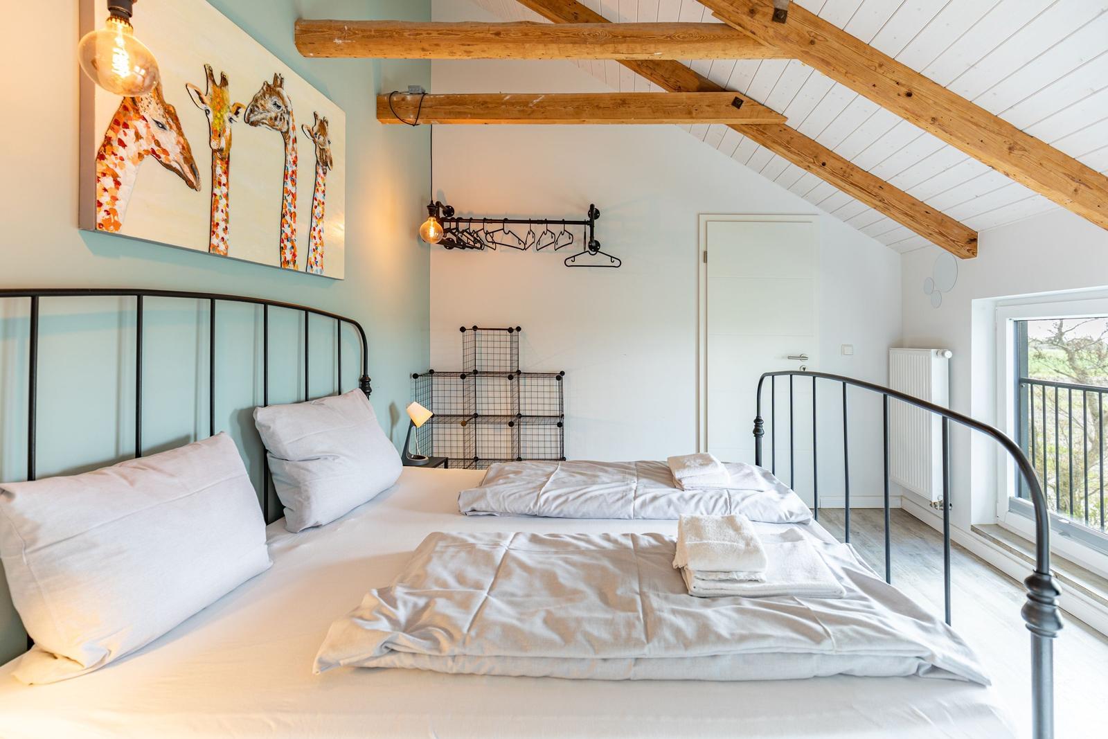 Schlafzimmer mit Doppelbett, Giraffenbild und Holzbalken an der Decke.