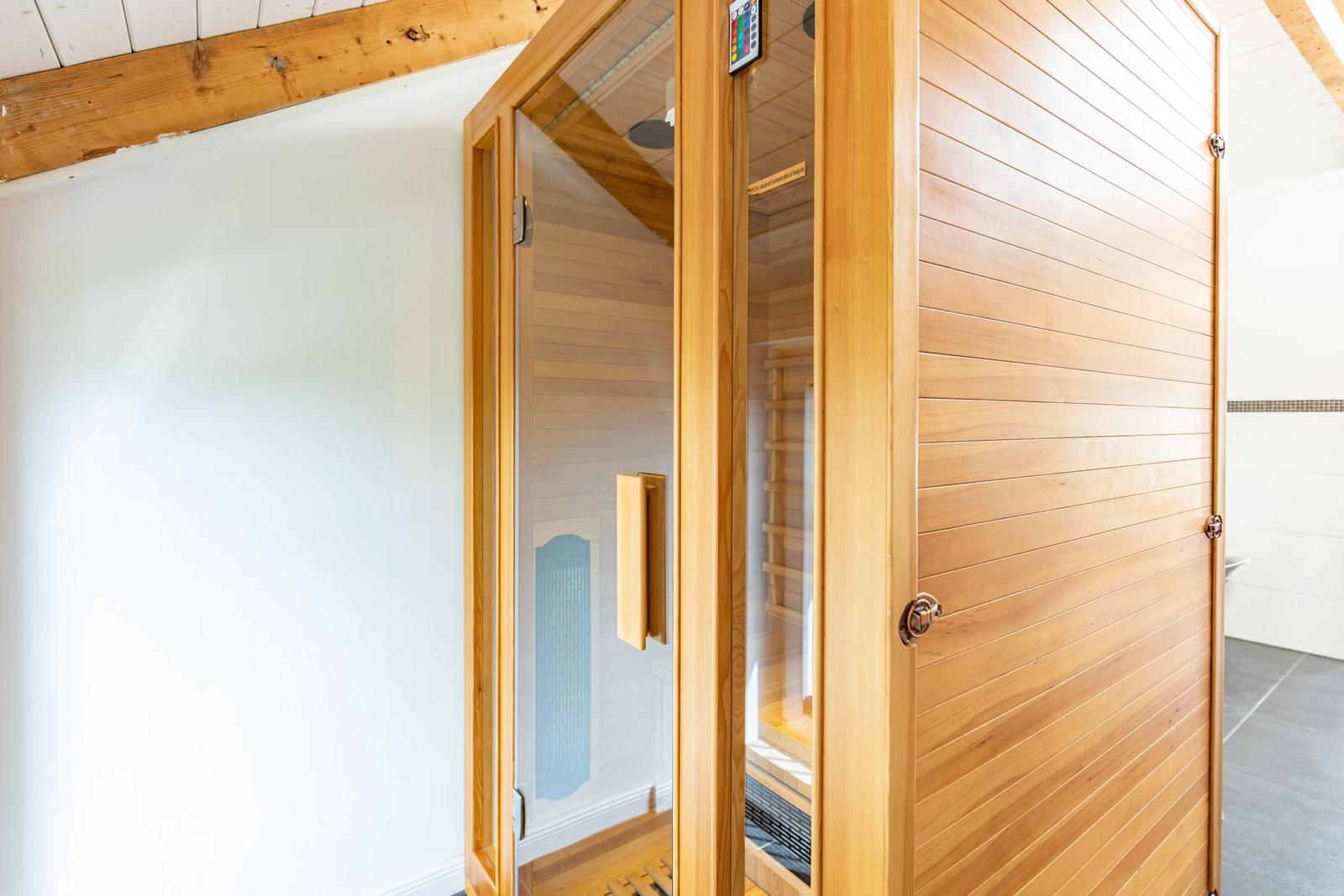 Eine Holzsauna mit Glasfront und Bedienfeld. Innere Holzwandung und Sitzbänke sichtbar.