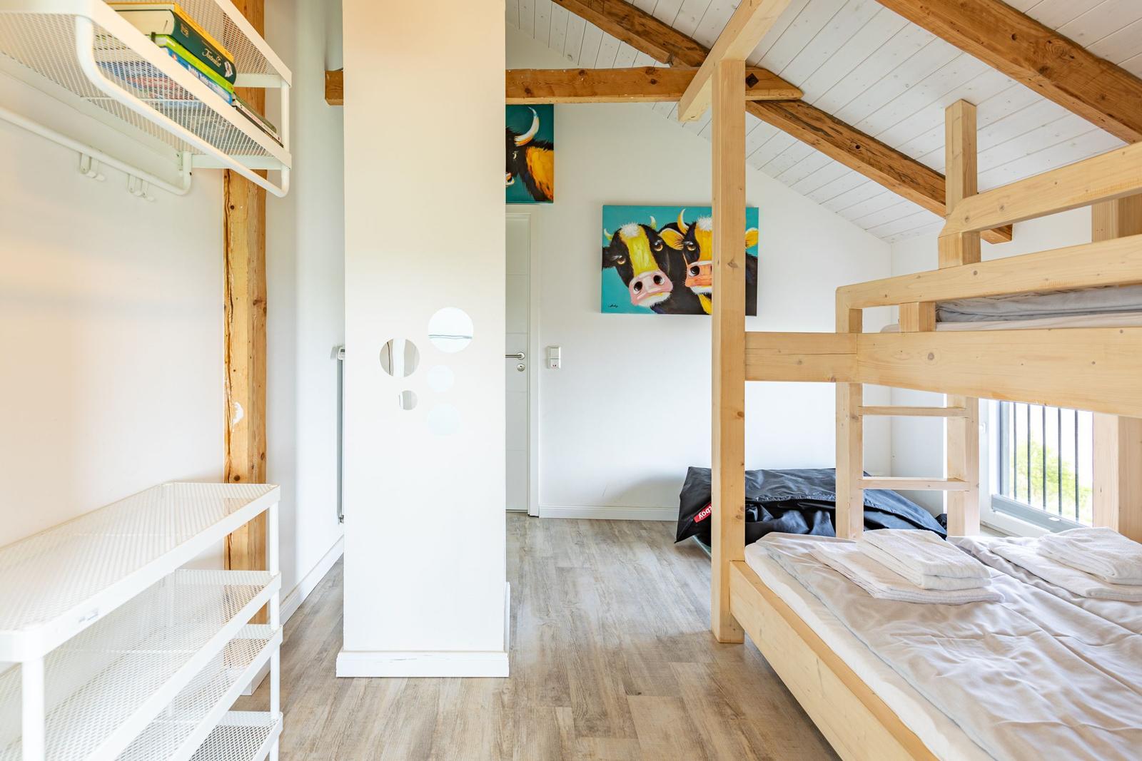 Zimmer mit Doppelstockbett, Holzbalkendecke und Wandbildern von Kühen.