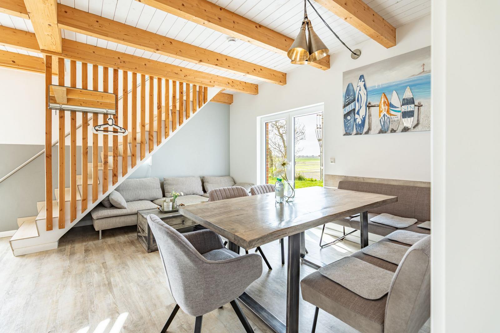 Essbereich mit Tisch, Stühlen und Sofa unter Holzbalkendecke. Treppenhaus links.