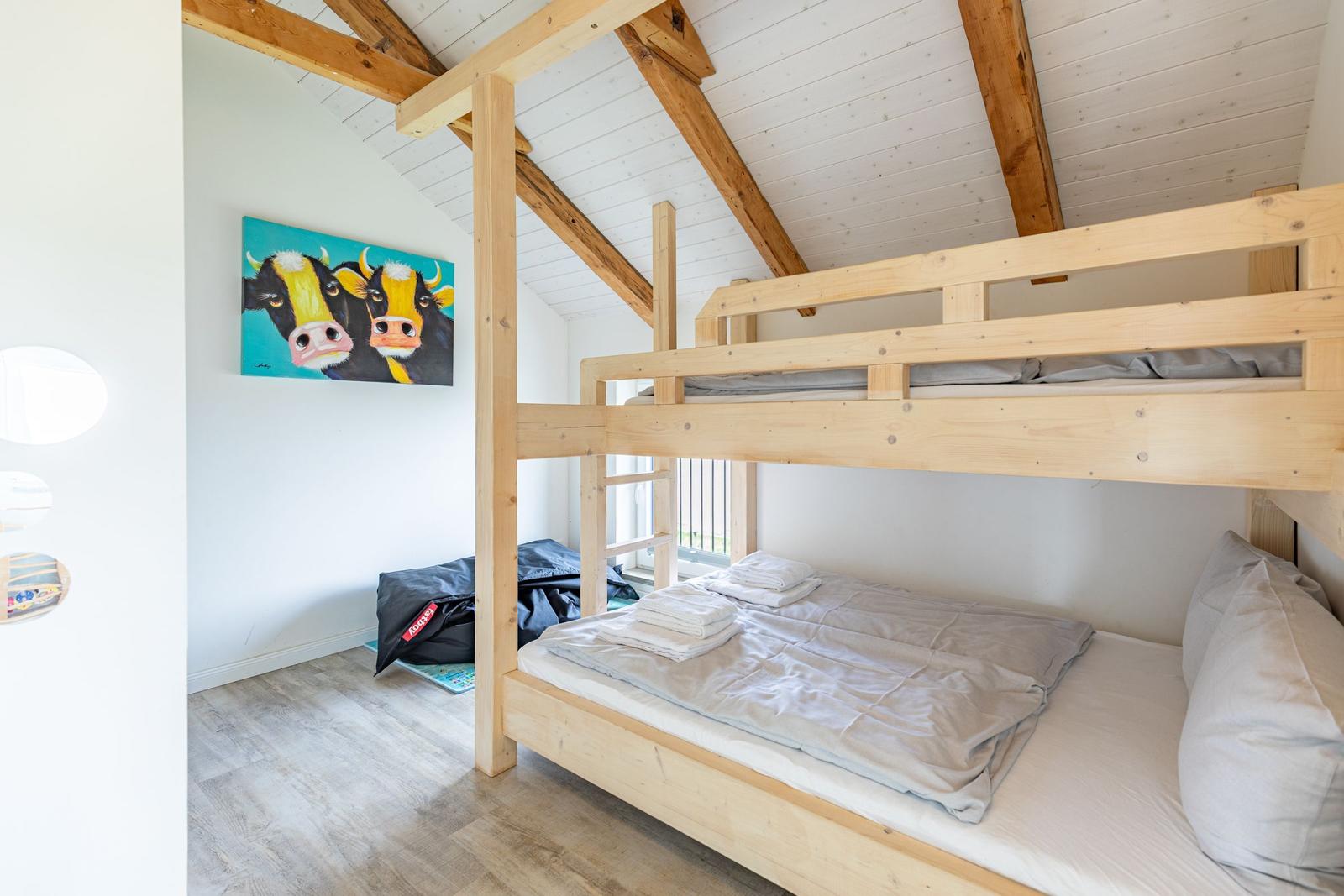 Zimmer mit Holzbett, Wandbild von Kühen und Holzbalkendecke.
