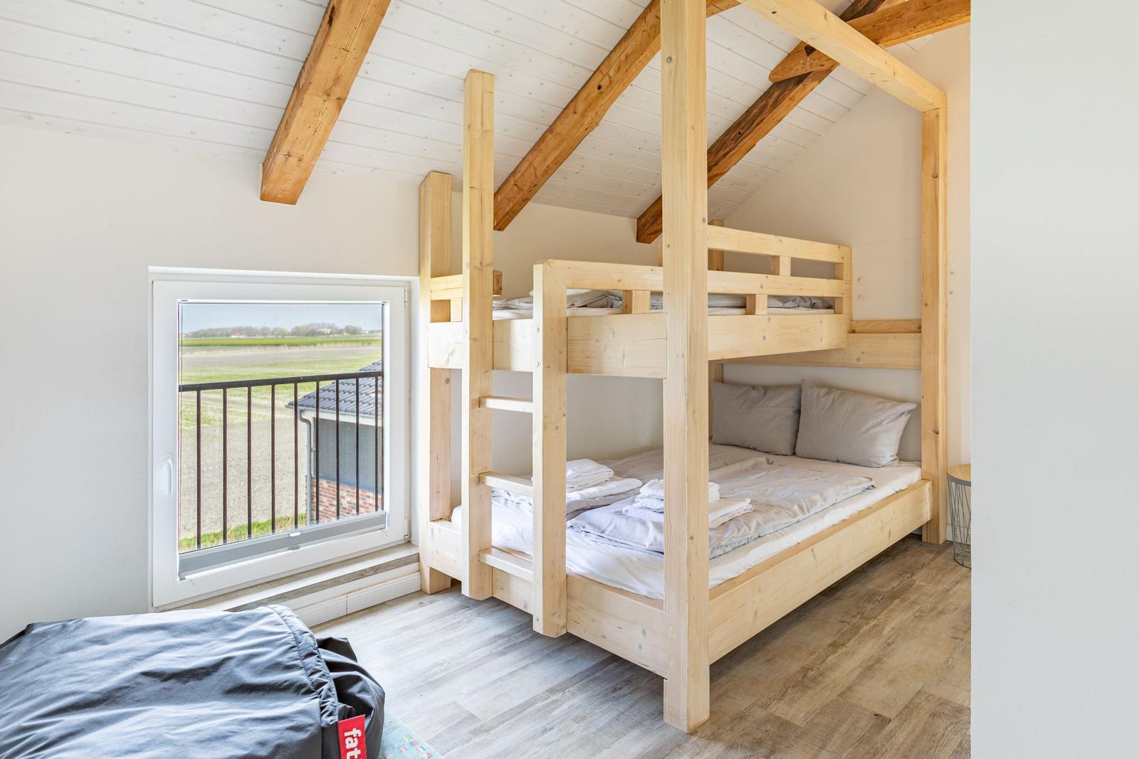 Zimmer mit Holzbett, Fenster und Sicht auf Feld