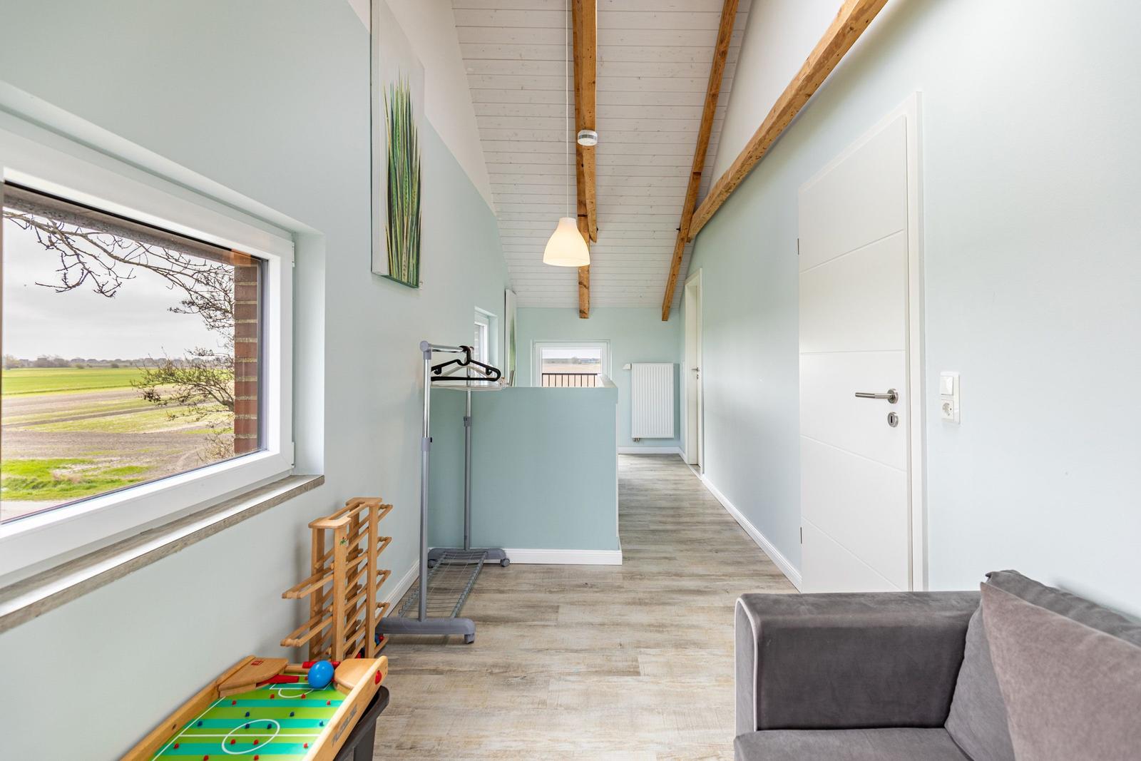 Flur mit Fenster, Sofa und Kinderzimmermöbel. Holzbalken an der Decke.