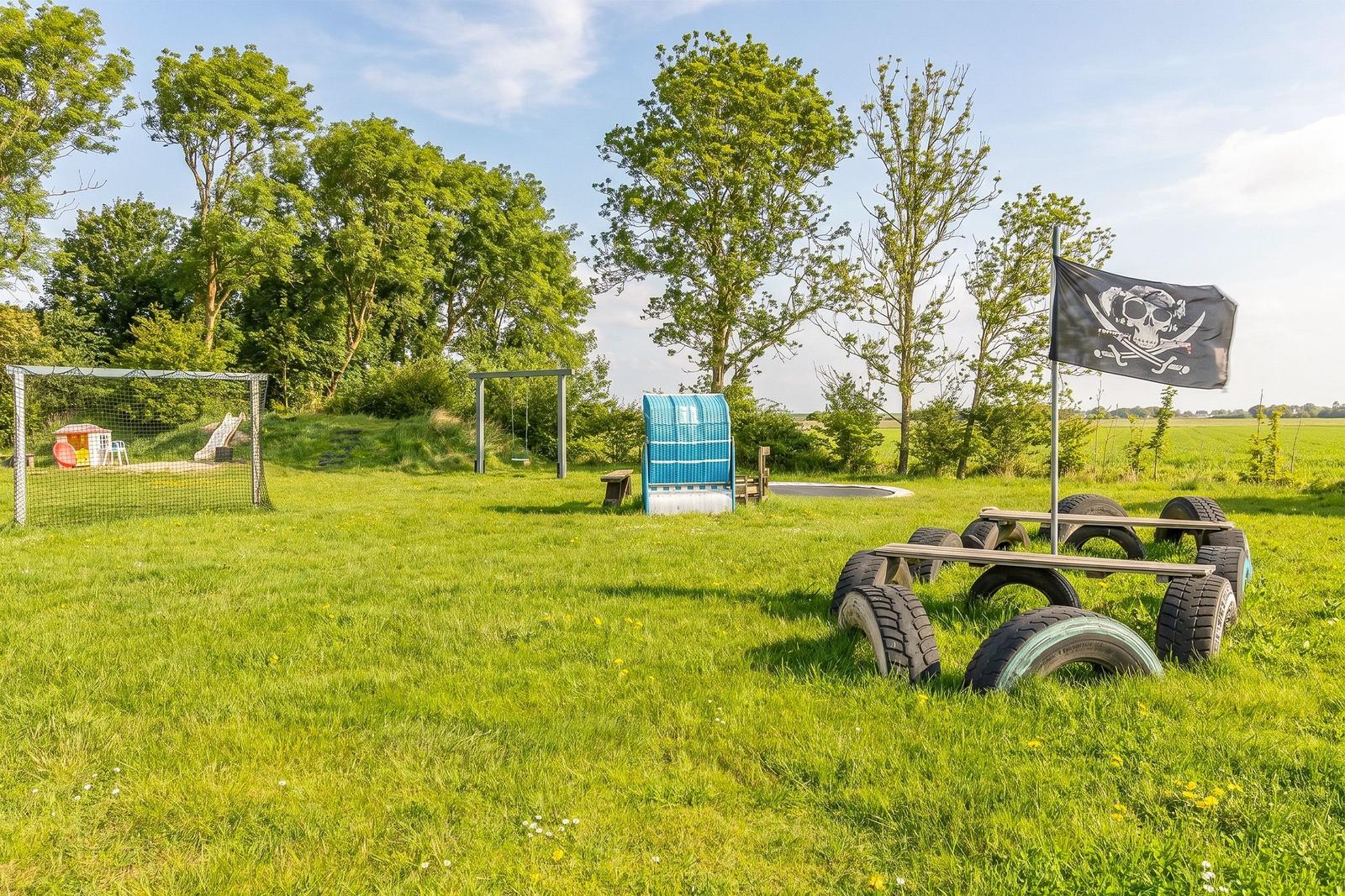 Grüner Spielplatz mit Klettergerüst, Schaukel und Piratenflagge. Spielplatz mit Sandkasten und Fußballtor.