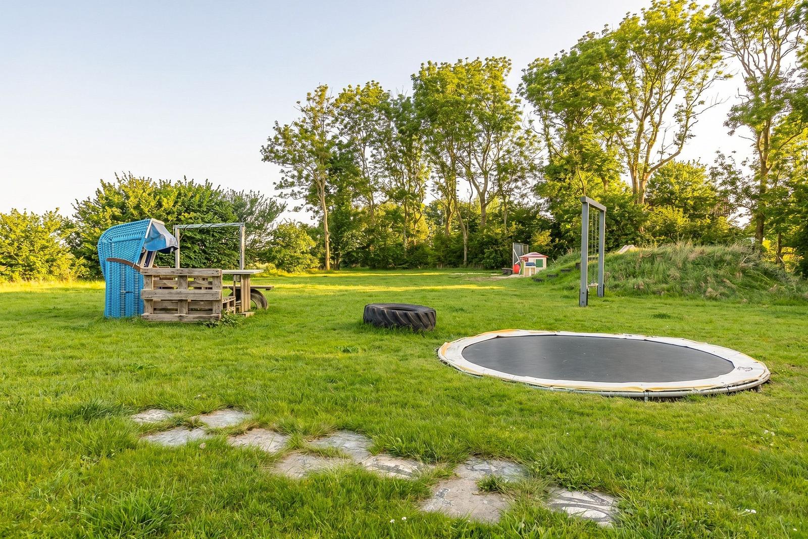 Grüner Garten mit Trampolin, Spielhaus und Steinweg. Hintergrund mit Bäumen.