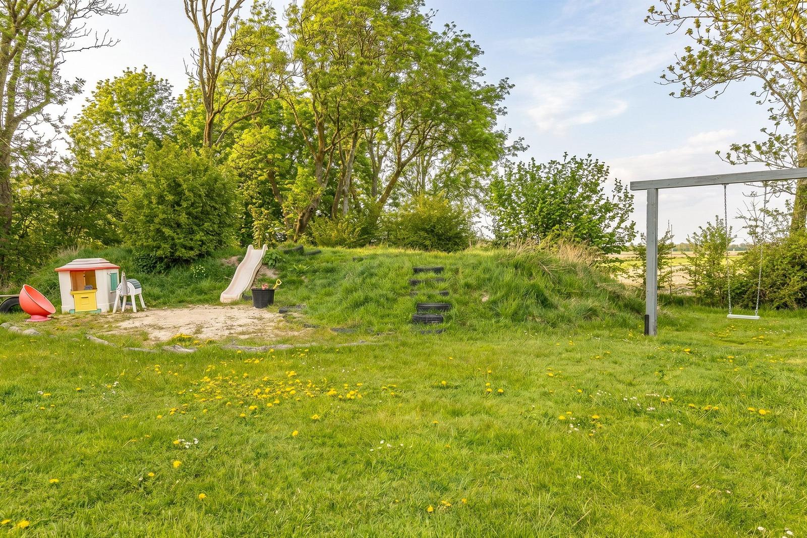 Grüner Garten mit Spielplatz, Rutsche und Schaukel. Spielhaus und Sandkasten sind vorhanden.