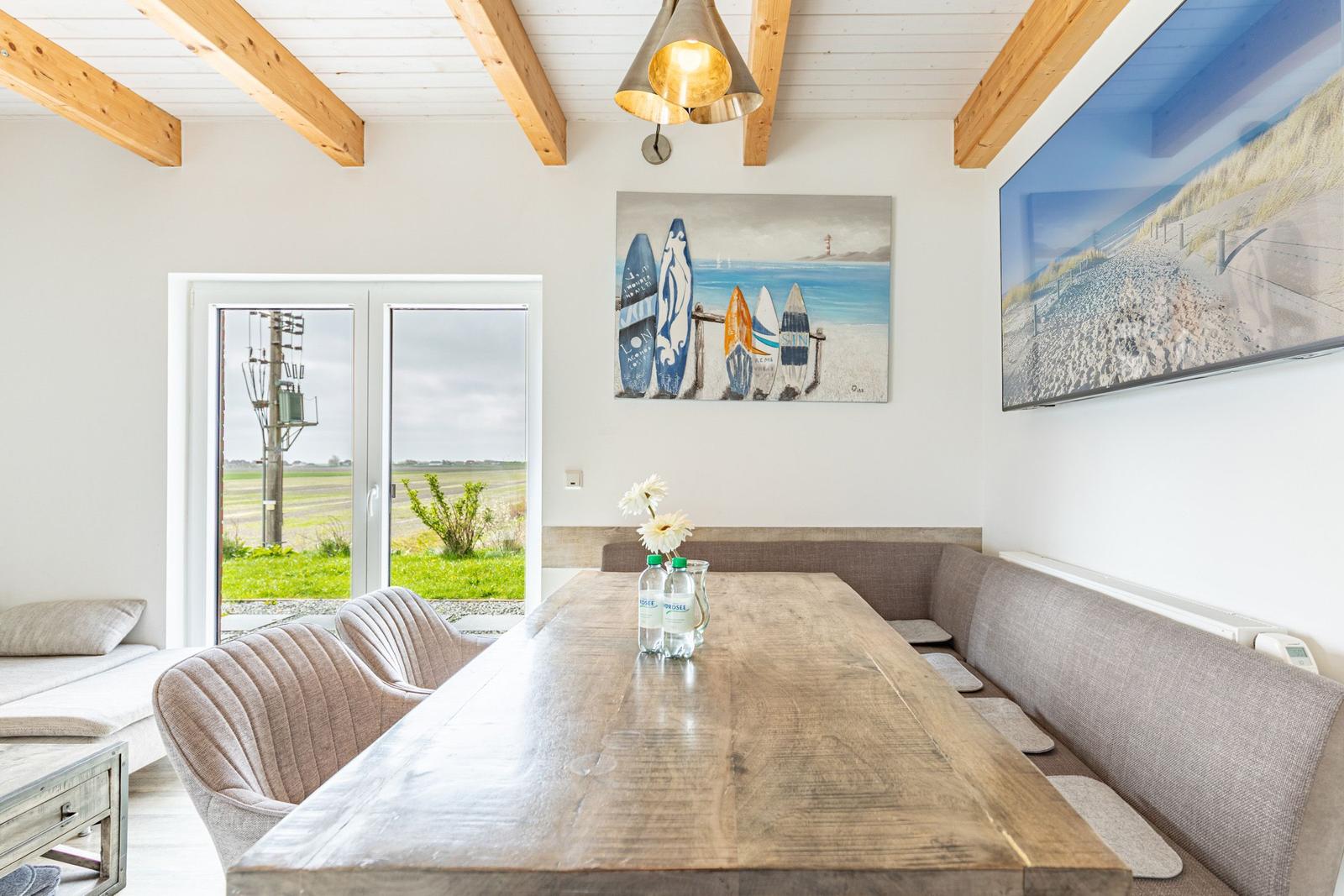 Esszimmer mit Holztisch, Sitzbank und Wandbildern. Durchgang zur Terrasse.