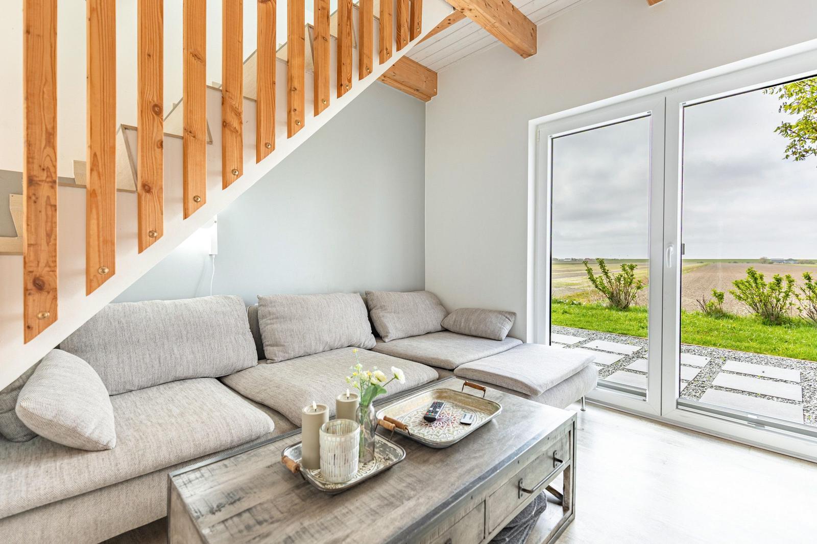 Wohnzimmer mit Sofa unter Treppe und Blick auf Feld durch Glastür