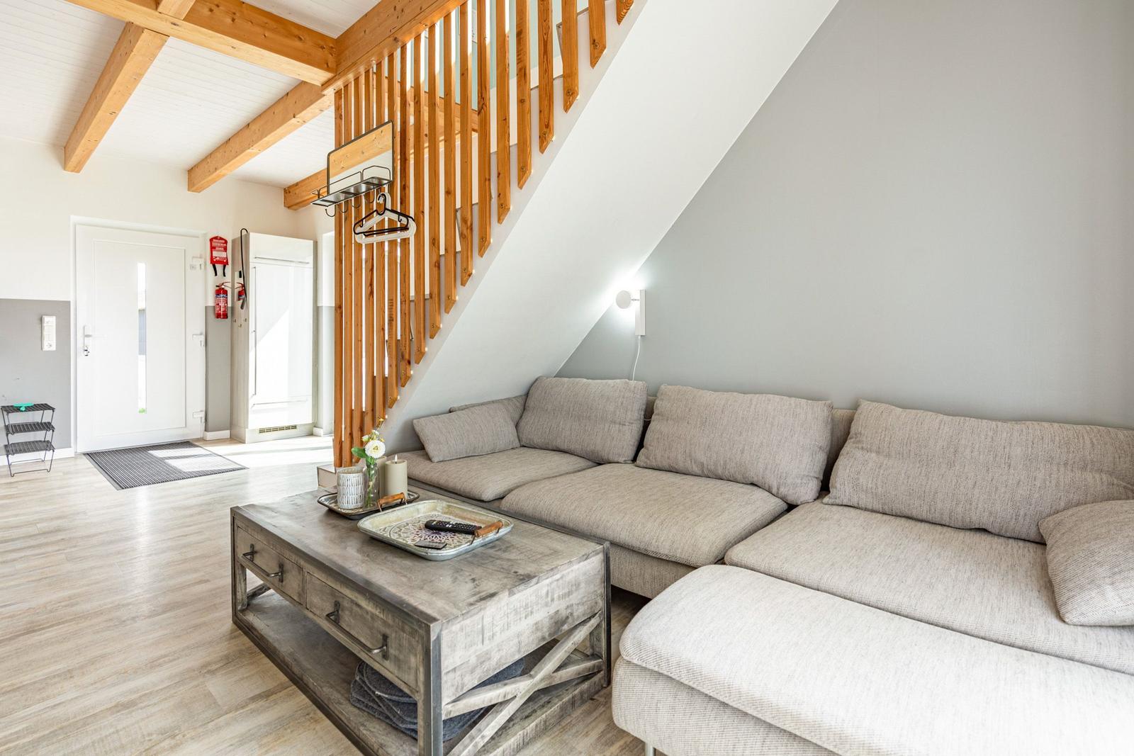 Wohnzimmer mit Sofa, Tisch und Holztreppe unter Dachschrägen.