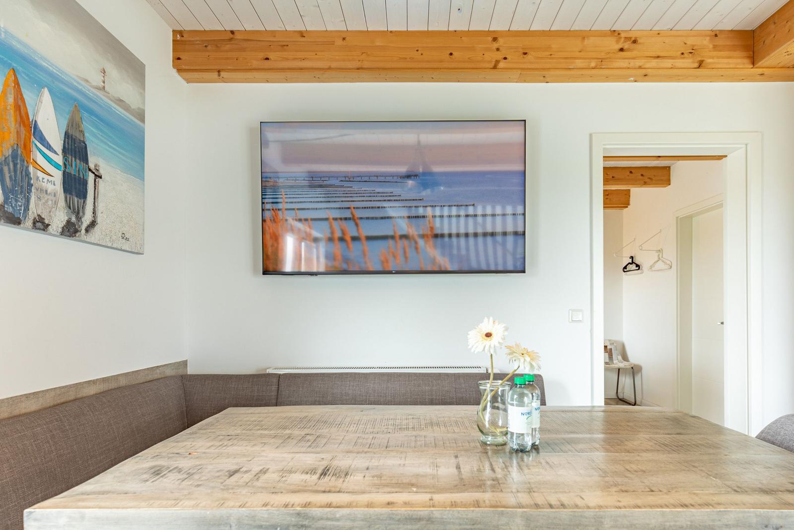 Esszimmer mit Holztisch, Sitzbank und Wandbildern. Fernseher an der Wand.