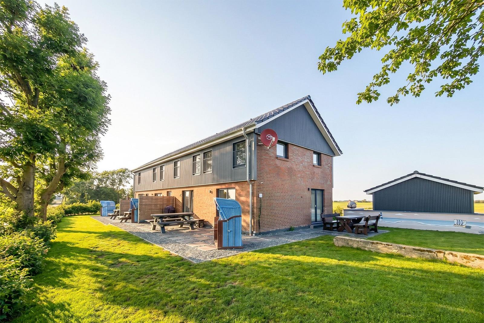 Moderne Ferienhaus mit Garten, Grillplatz und Pool. Holztische und Stühle im Freien.