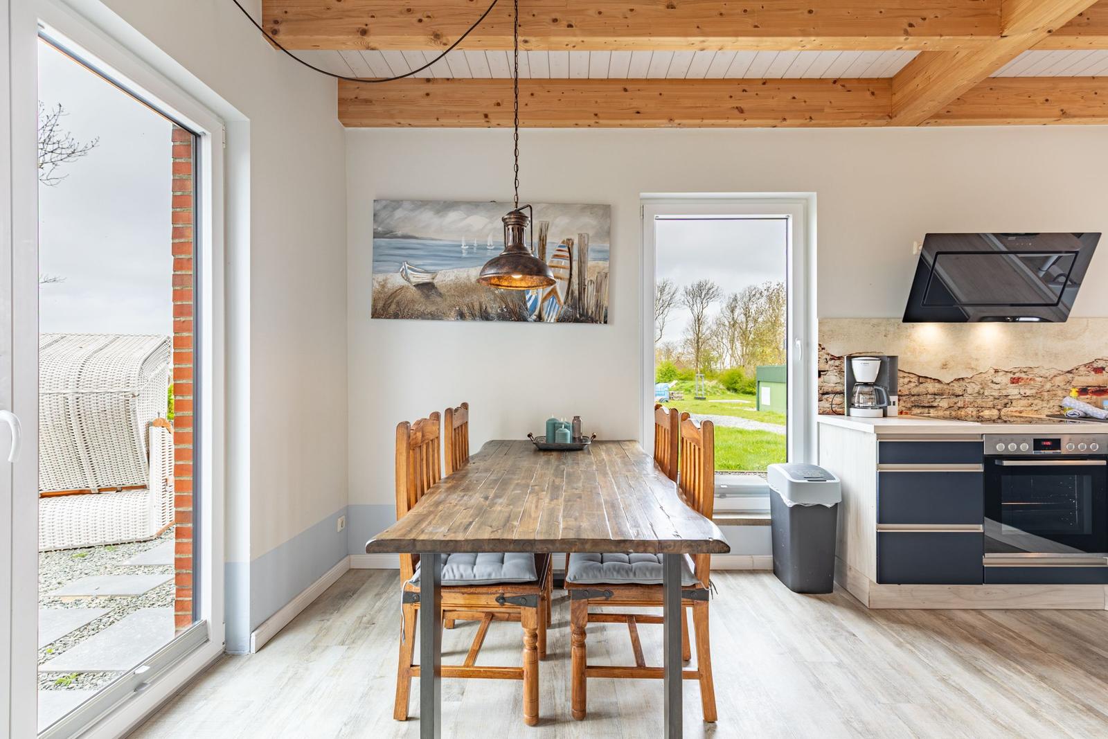 Essbereich mit Holztisch, Stühlen und Küchenzeile. Holzdecke und Fenster zur Außenterrasse.