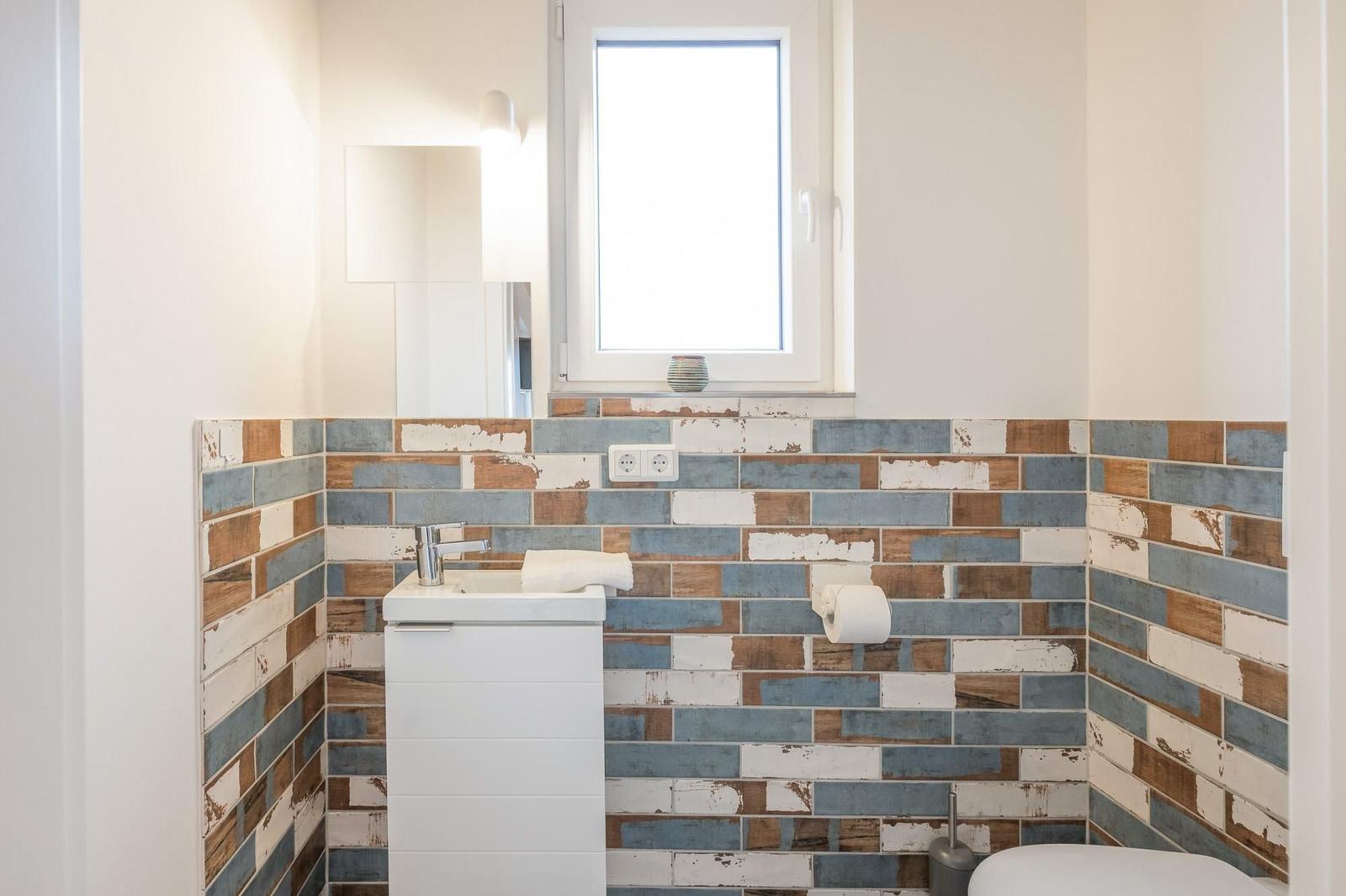 Badezimmer mit farbigen Fliesen, Waschbecken und Fenster.