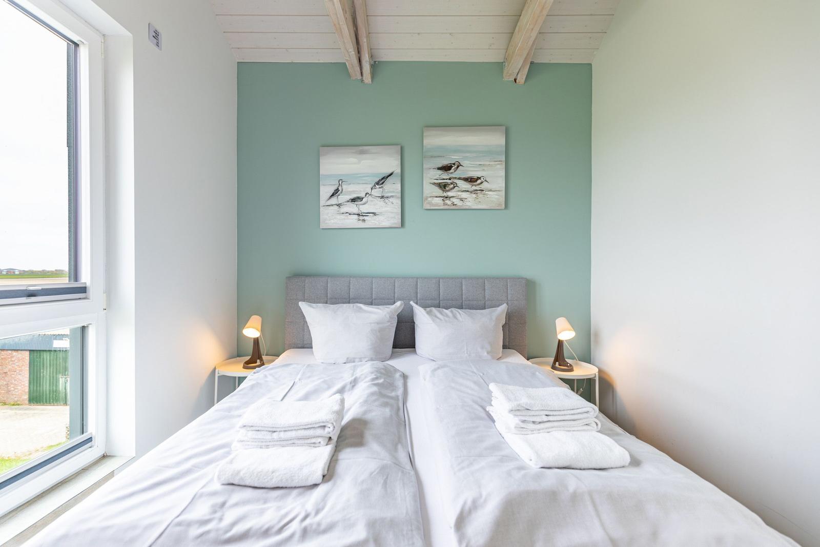Schlafzimmer mit Bett, zwei Nachttischen und Fenster. Wand mit zwei Bildern.