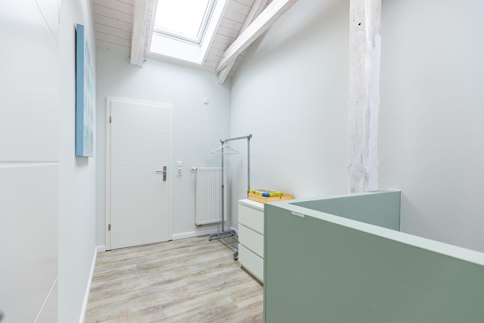 Raum mit Holzboden, weißer Tür und Dachfenster. Kleiderständer und Schrank sind vorhanden.