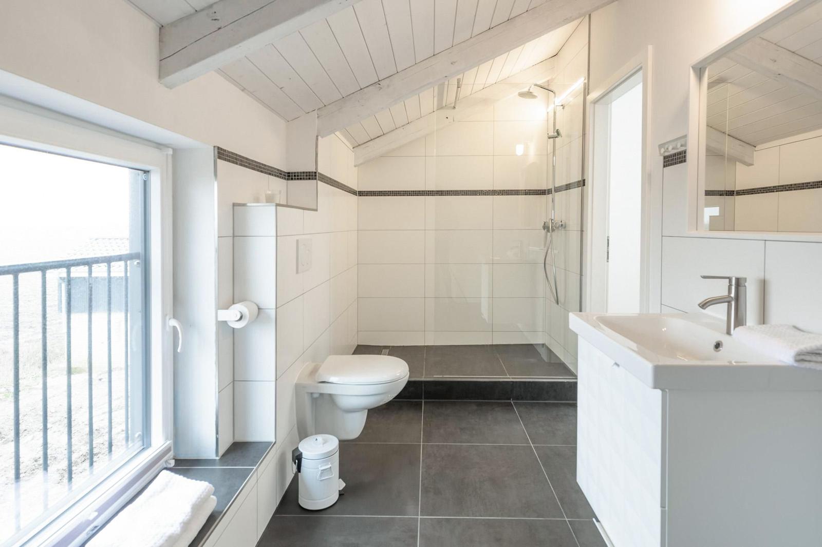 Badezimmer mit Dusche, WC und Waschbecken. Fenster mit Blick auf Balkon.