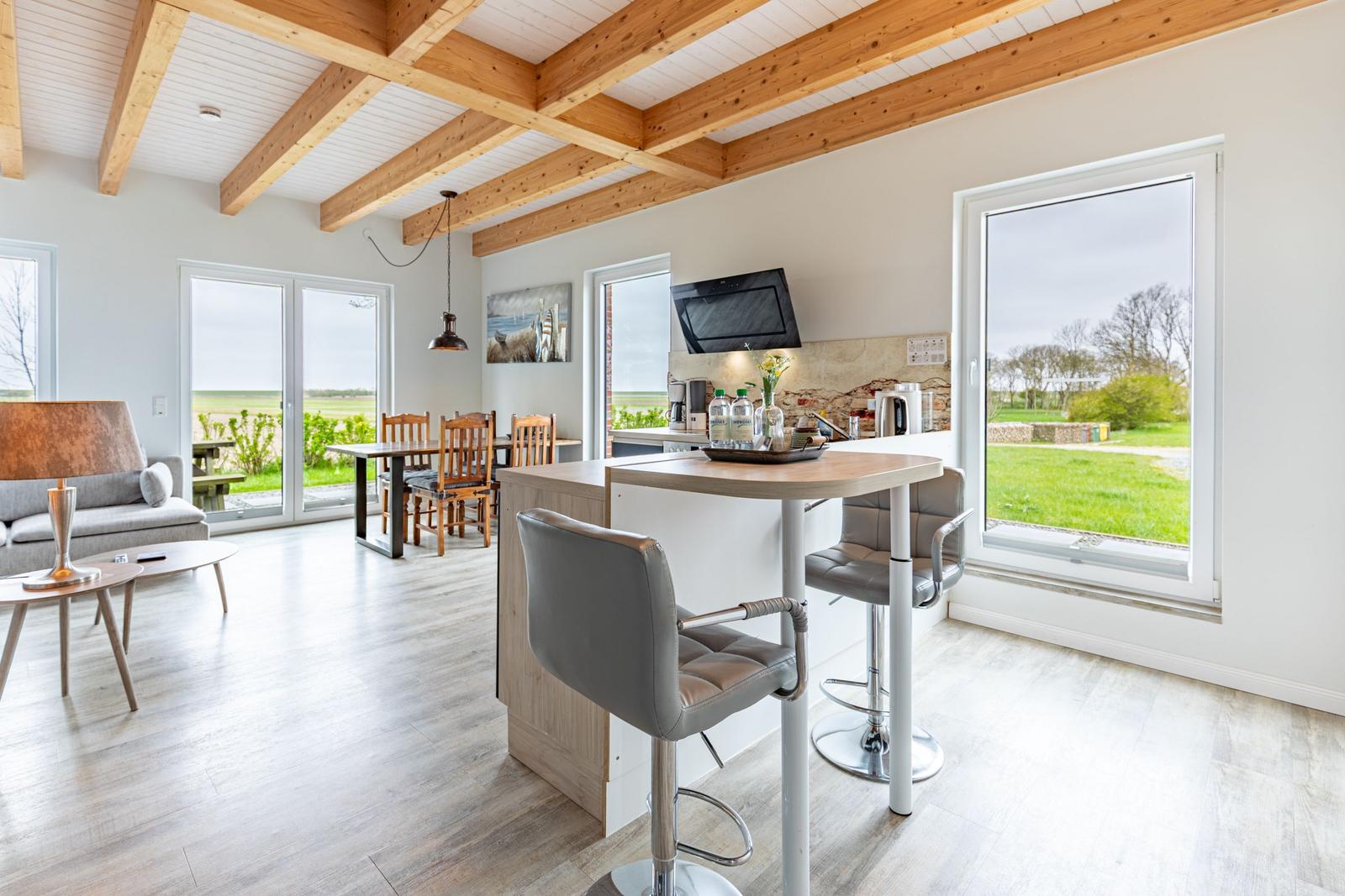 Küche mit Barhocker, Essbereich und Wohnzimmer mit Holzbalkendecke und Blick auf die Landschaft.