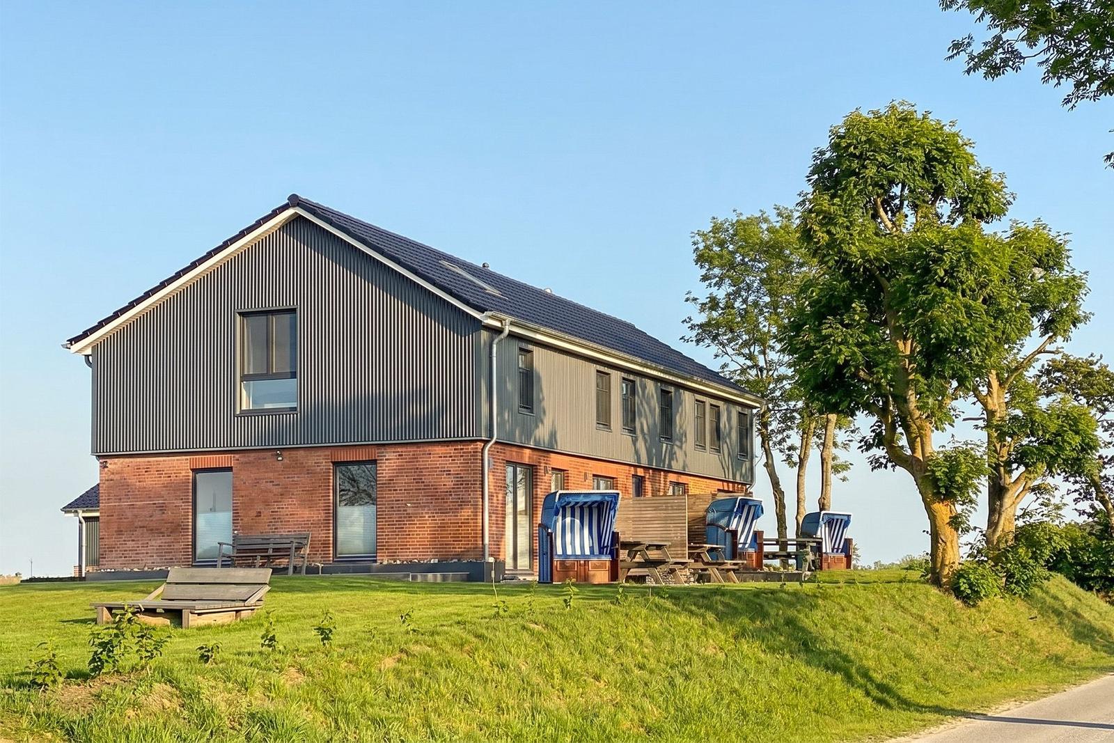 Moderne Ferienhaus mit Terrasse, Strandkörben und grünem Rasenbereich.