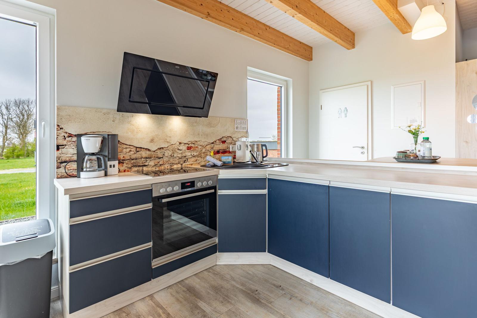 Küche mit blauen Schränken, Steinwand und Holzbalken an der Decke.
