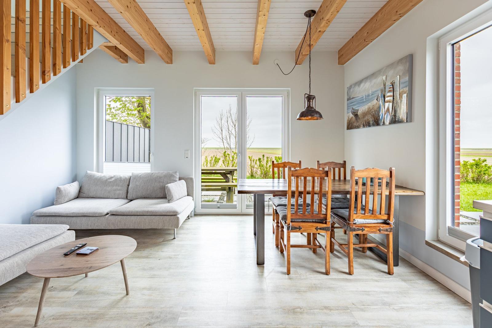 Wohn- und Essbereich mit Holzdecke, Sofa, Tisch und Stühlen sowie großen Fenstern.