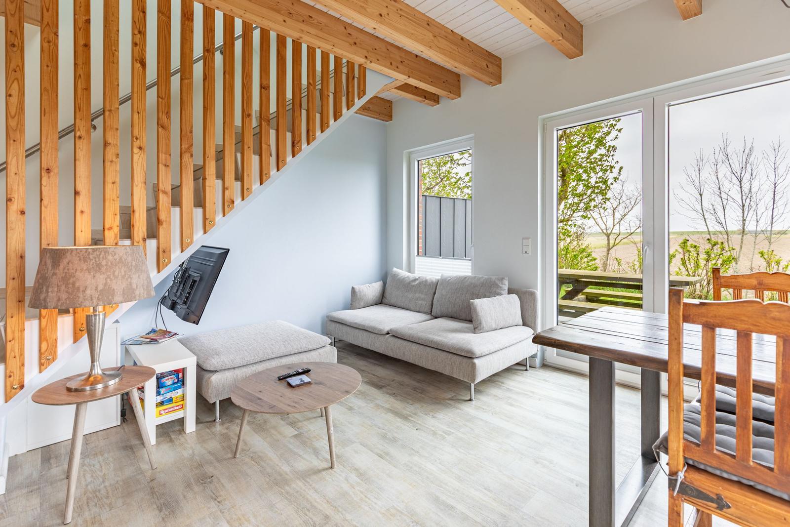 Wohnbereich mit Sofa, Tisch und Stühlen. Holzstufen und große Fenster.