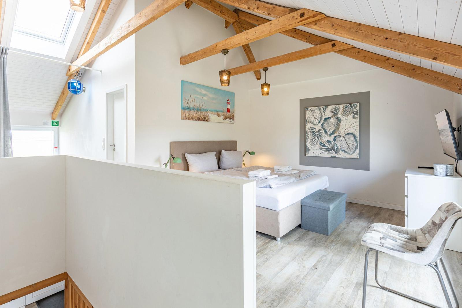 Schlafzimmer mit Dachschrägen, Bett, Stuhl und Wandbildern.