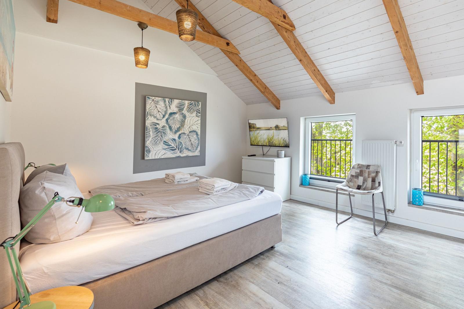 Schlafzimmer mit Bett, Fernseher und Fenstern zum Balkon