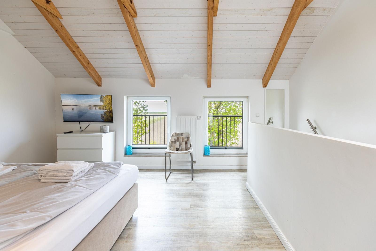 Schlafzimmer mit Bett, Fernseher und zwei Fenstern mit Blick auf Balkon.