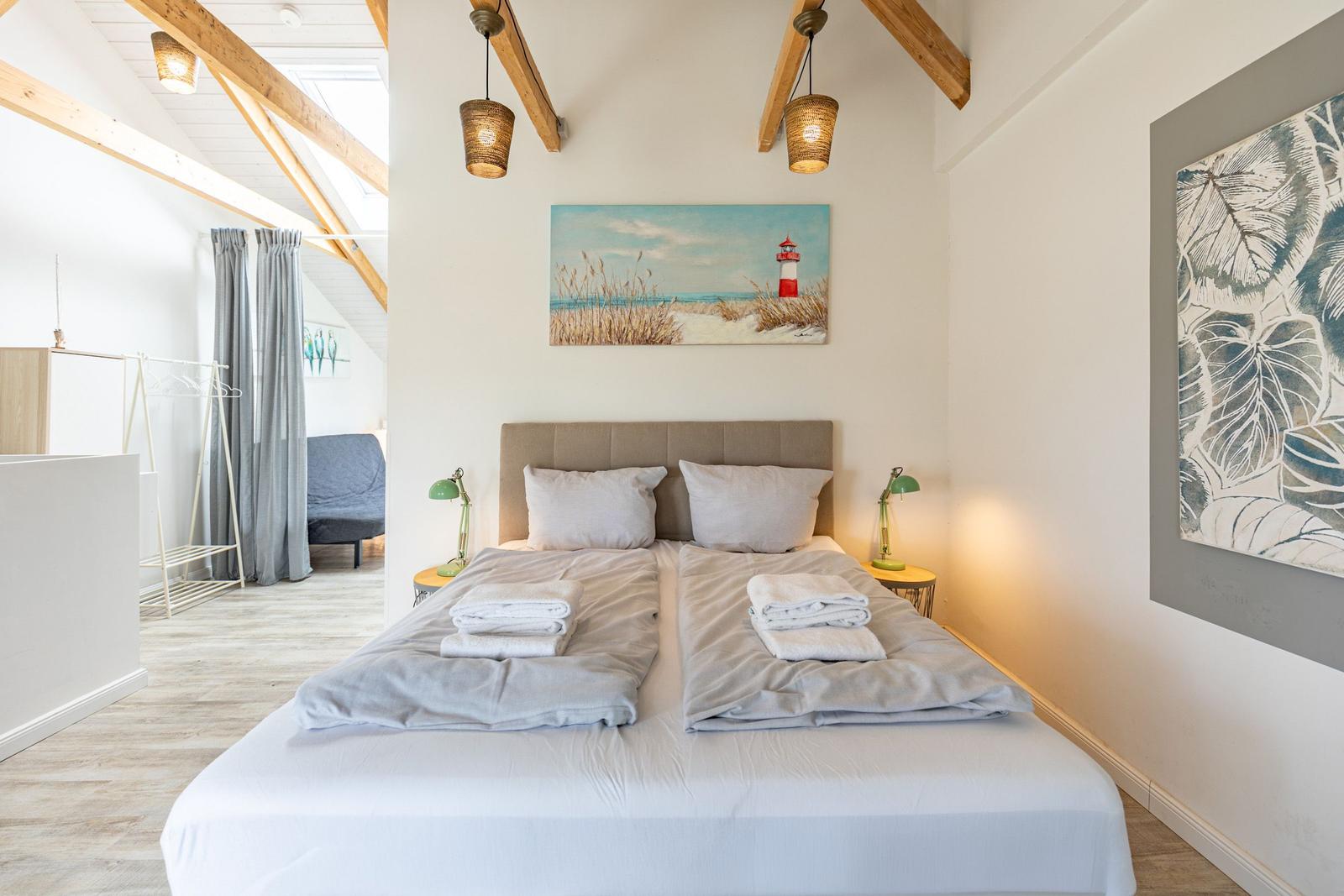 Doppelbett mit Handtüchern, Wandbilder und Holzbalken an der Decke.