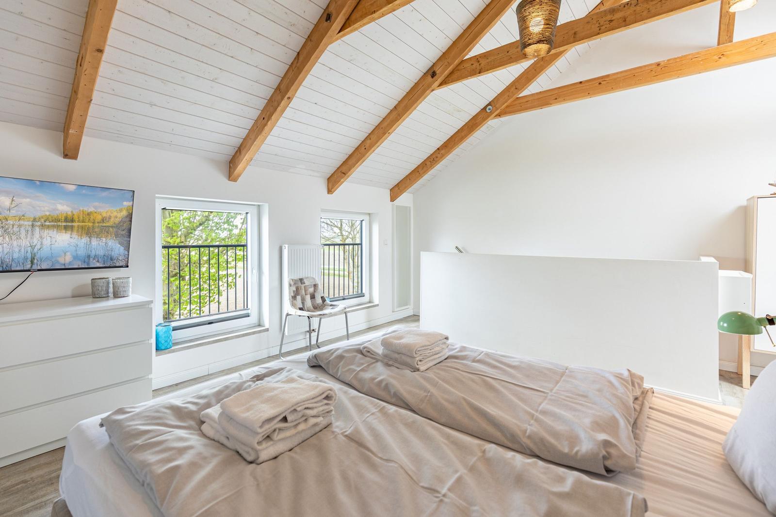 Schlafzimmer mit Doppelbett, TV und Balkonfenstern unter Holzbalkendecke.