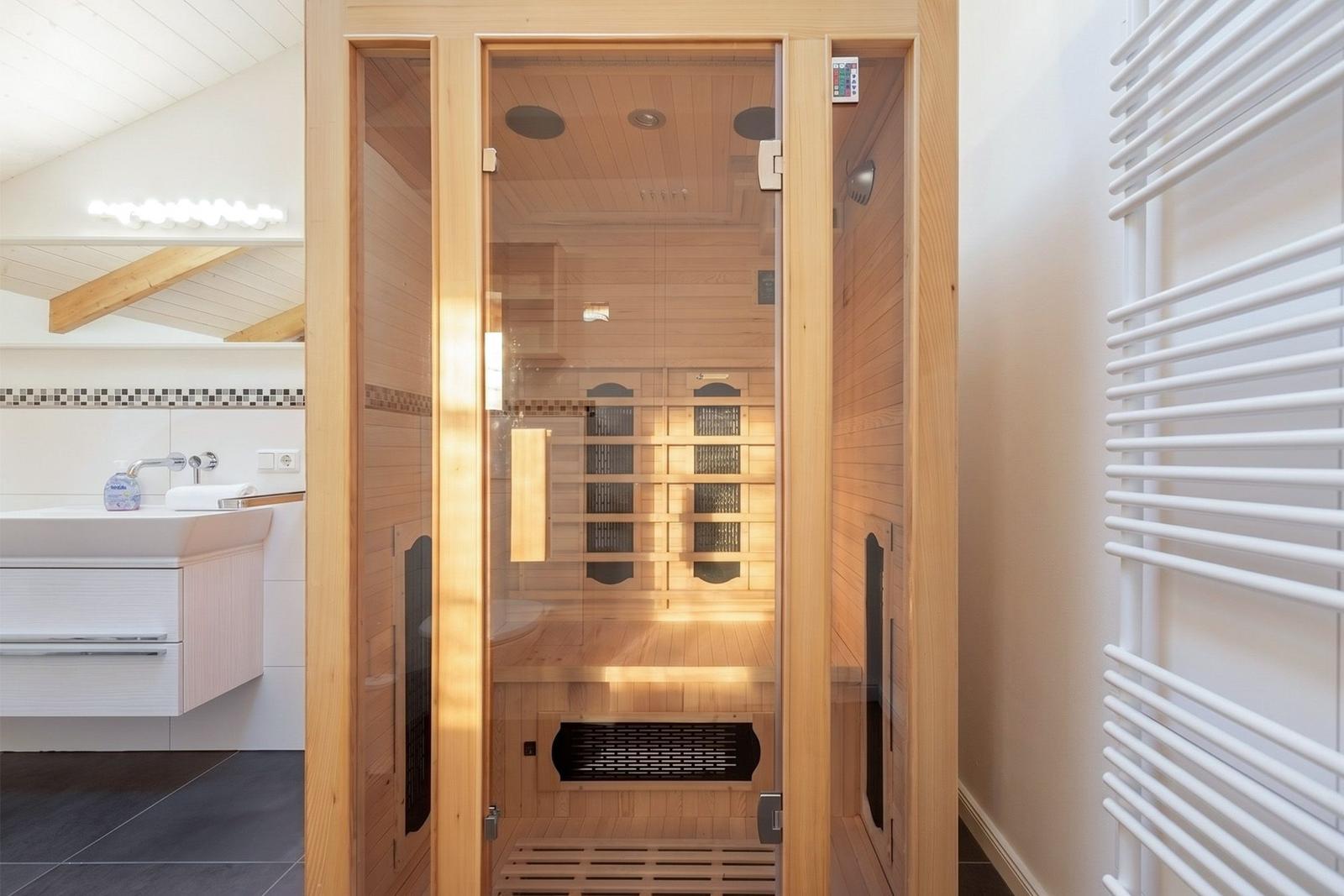 Sauna mit Holzverkleidung und Glasfront. Neben dem Waschbecken ist eine Heizung angebracht.