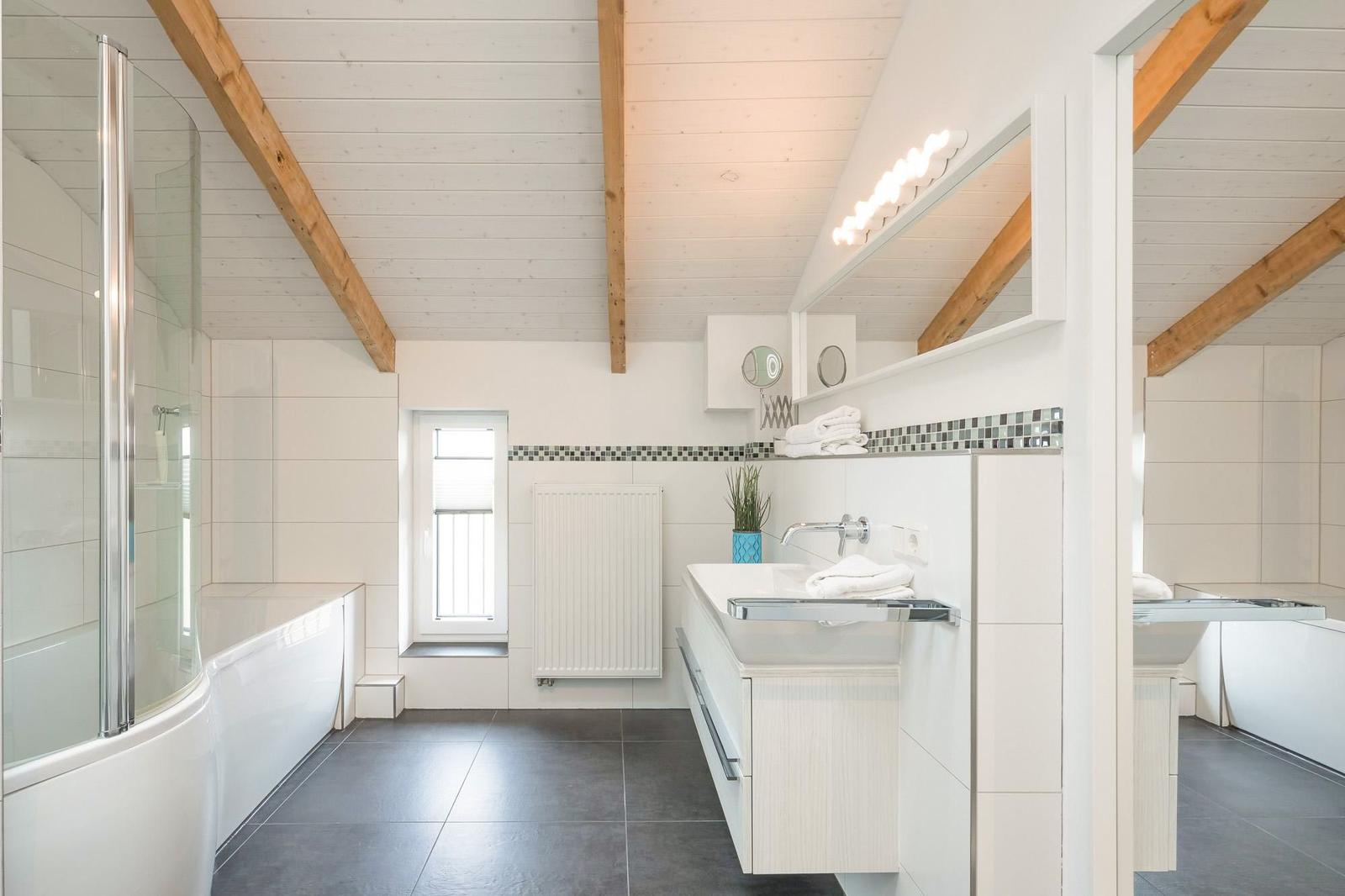 Badezimmer mit Dusche, Waschbecken und Fenster. Holzbalken an der Decke.