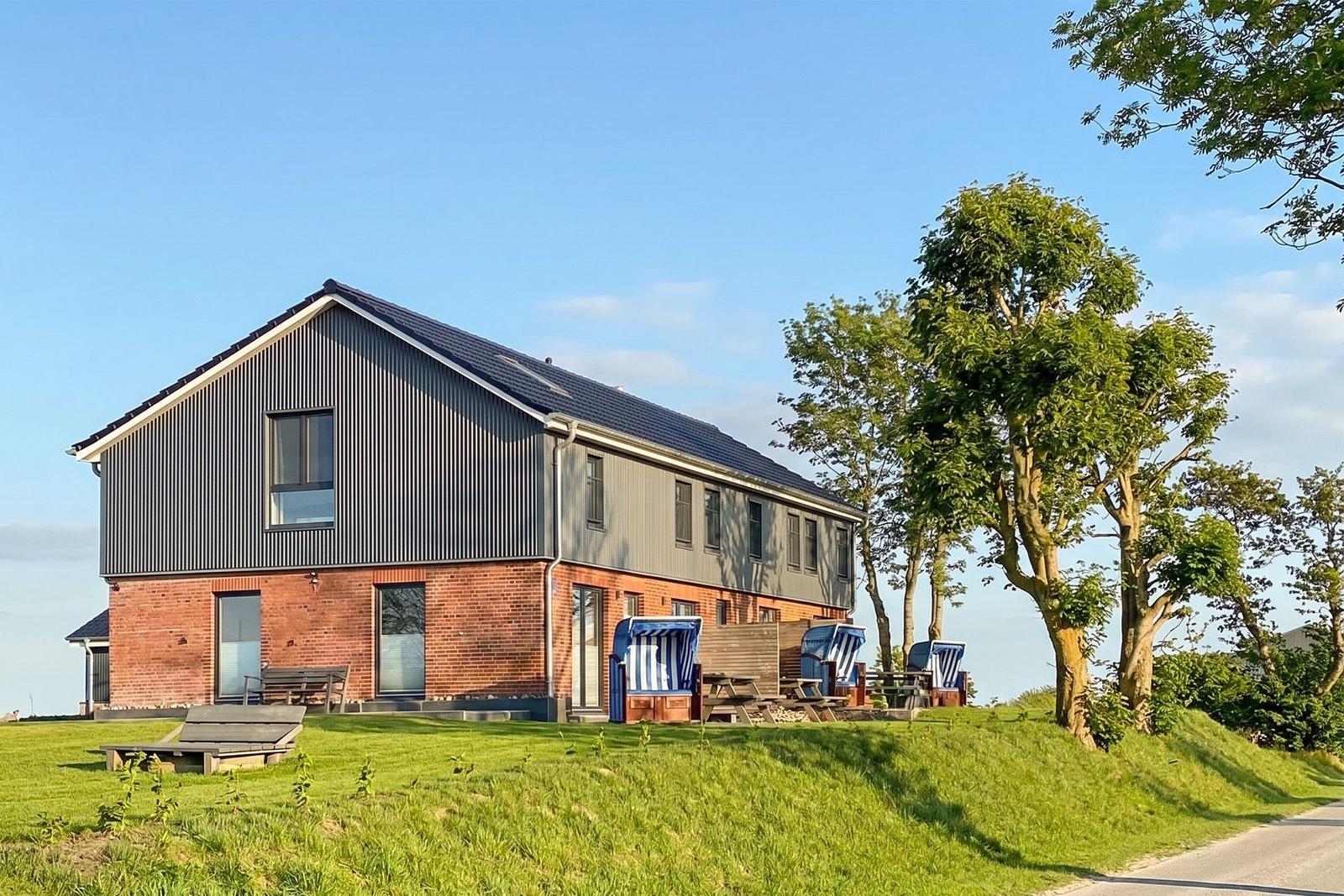 Moderne Villa mit Holzterrasse und Strandkörben auf grünem Grund.