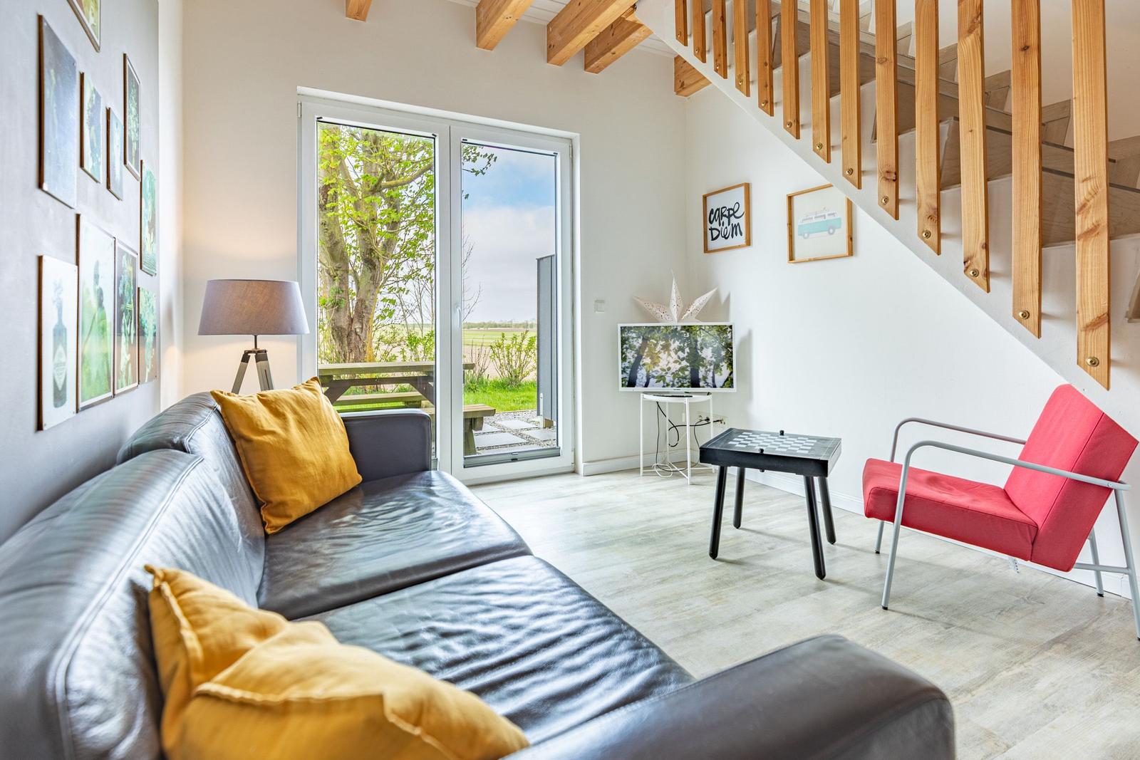 Wohnzimmer mit Sofa, roter Sitzgelegenheit und Terrassentür zum Garten.