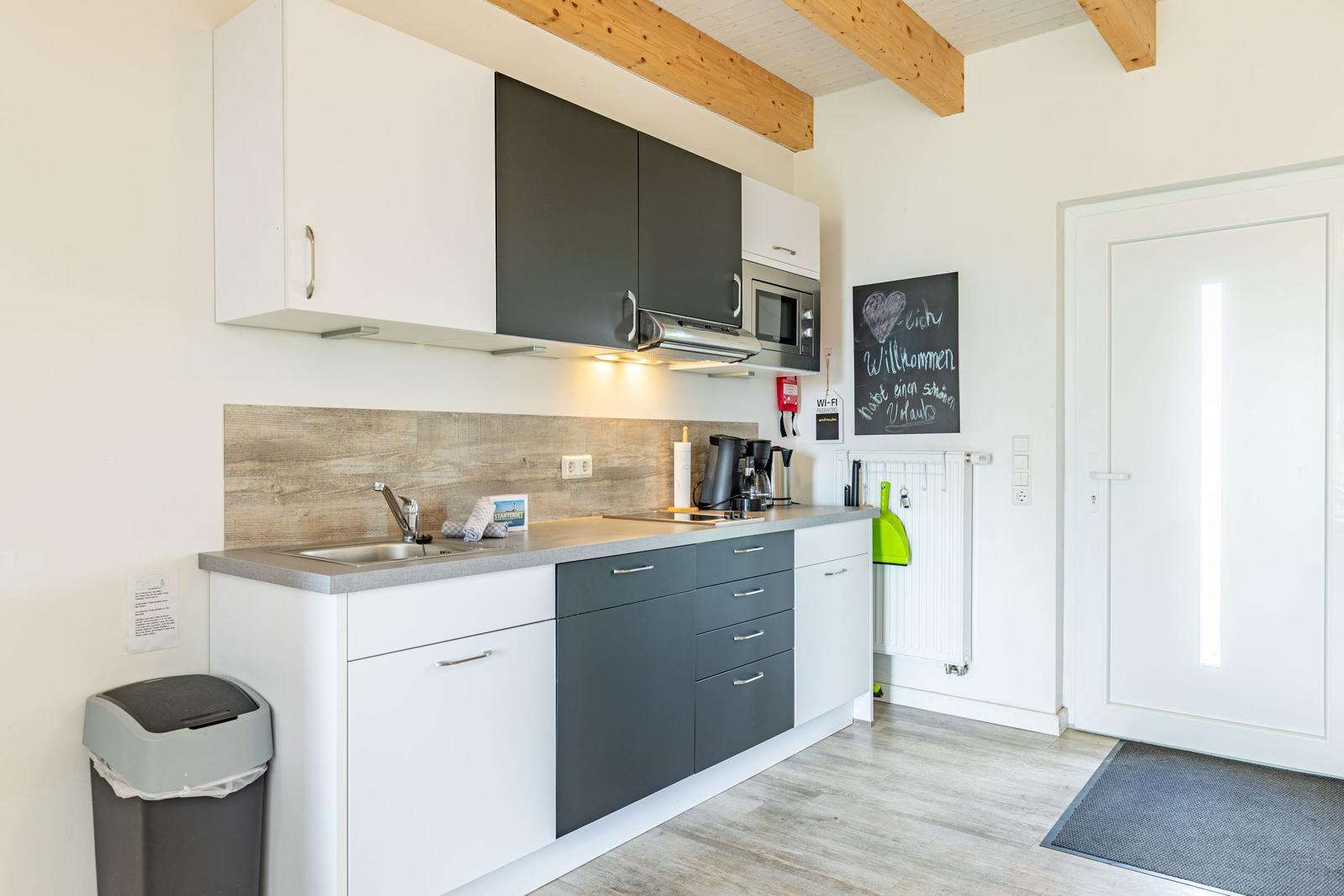 Küche mit weißen und grauen Schränken, Holzbalken an der Decke und einer Tür rechts.