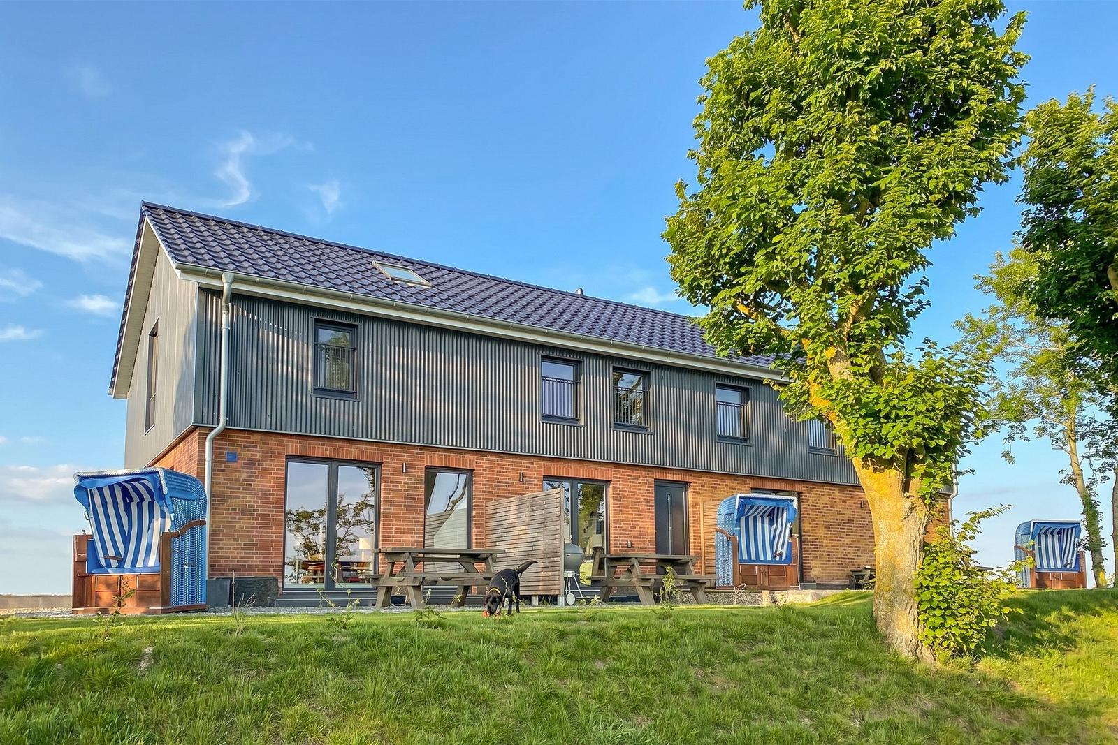 Moderne Ferienhaus mit Terrasse, Picknicktischen und Strandkörben im Grünen.