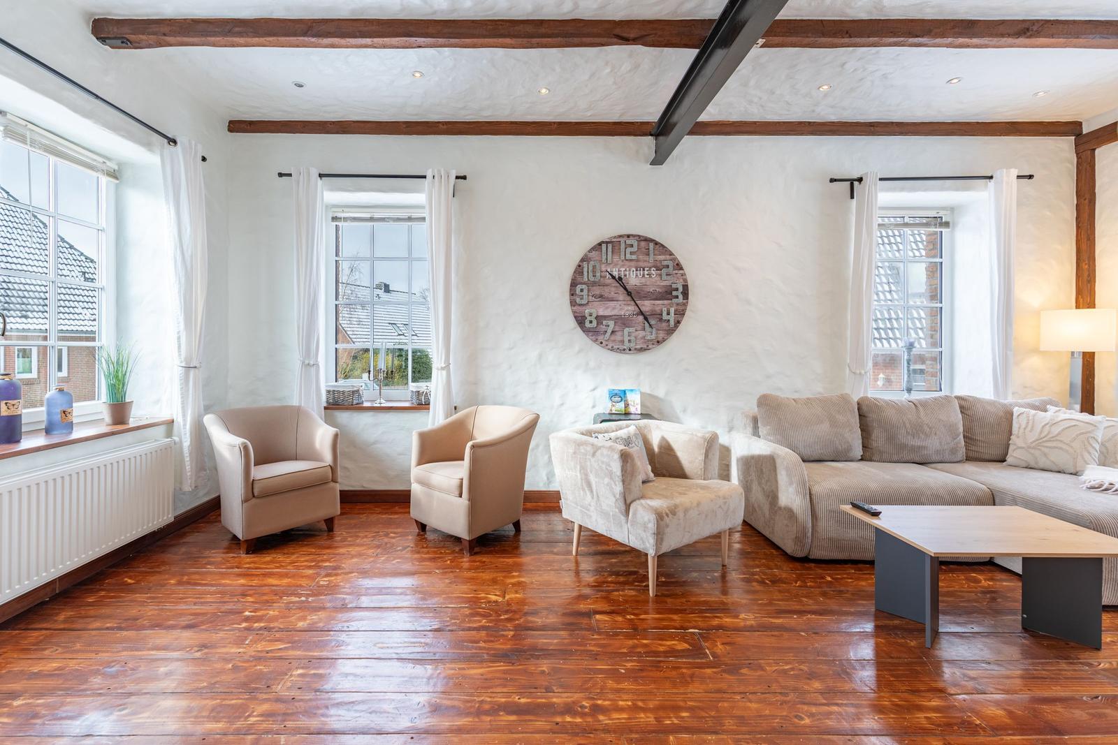 Living room with hardwood floor, sofa, armchairs, and wall clock.