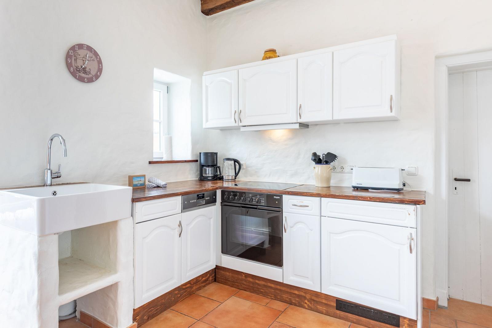 Kitchen with white cabinets, wooden surfaces, and oven. Wall clock and window visible.
