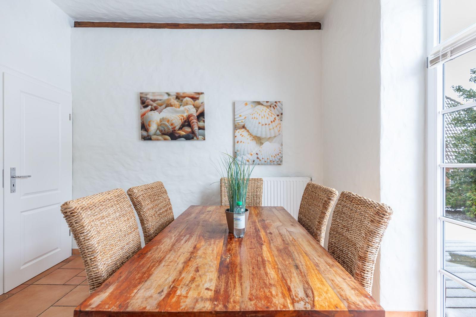 Dining room with wooden table, wicker chairs, and seashell pictures on the wall.