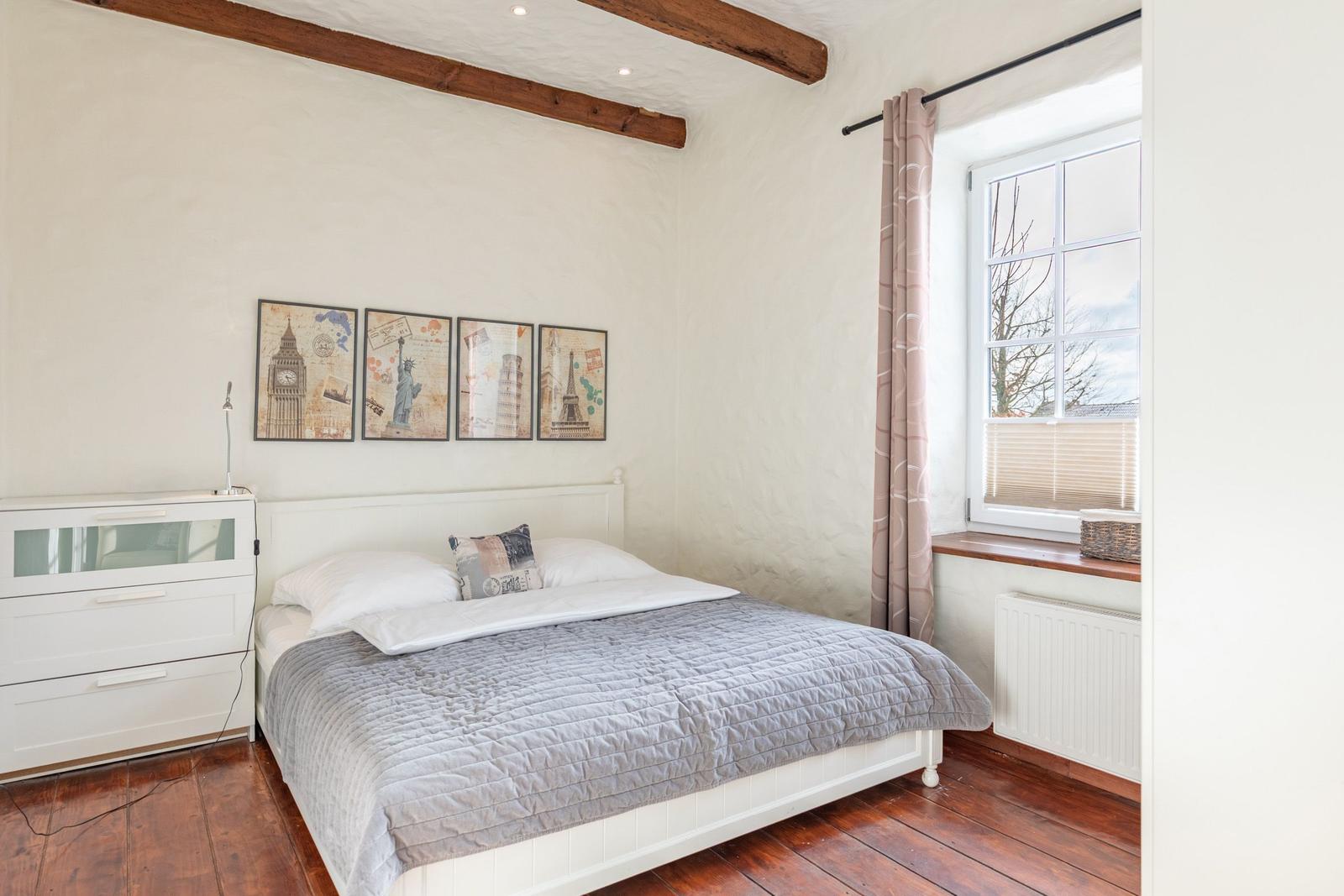Bedroom with bed, dresser, and window. Wall art shows landmarks.