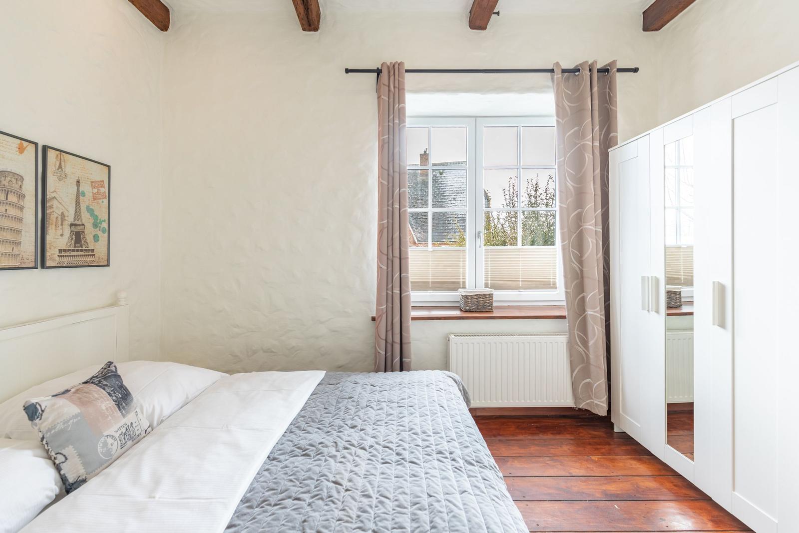 Bedroom with bed, window, and wardrobe. Wooden floor and ceiling beams.