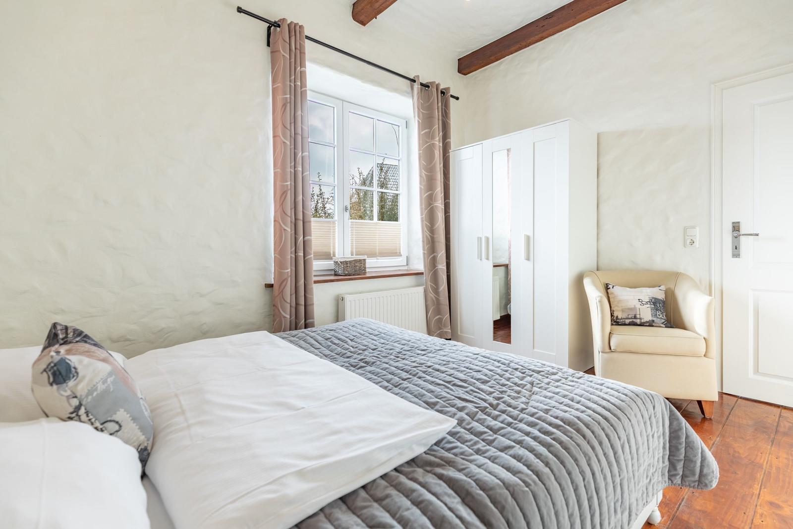 Bedroom with bed, window, wardrobe, and armchair.