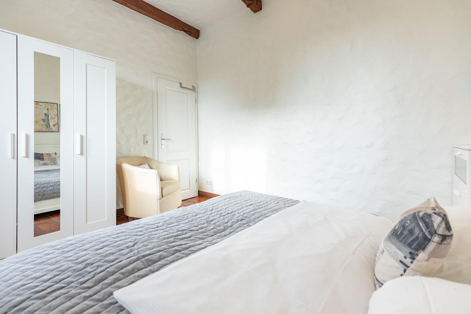 Bedroom with bed, wardrobe, and armchair. Ceiling with wooden beams.